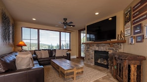 A living room with a fireplace, a large flat-screen TV, a ceiling fan, and a stone fireplace surround. - Purgatory Lodge 405 - Managed by Purgatory Resort (Durango)