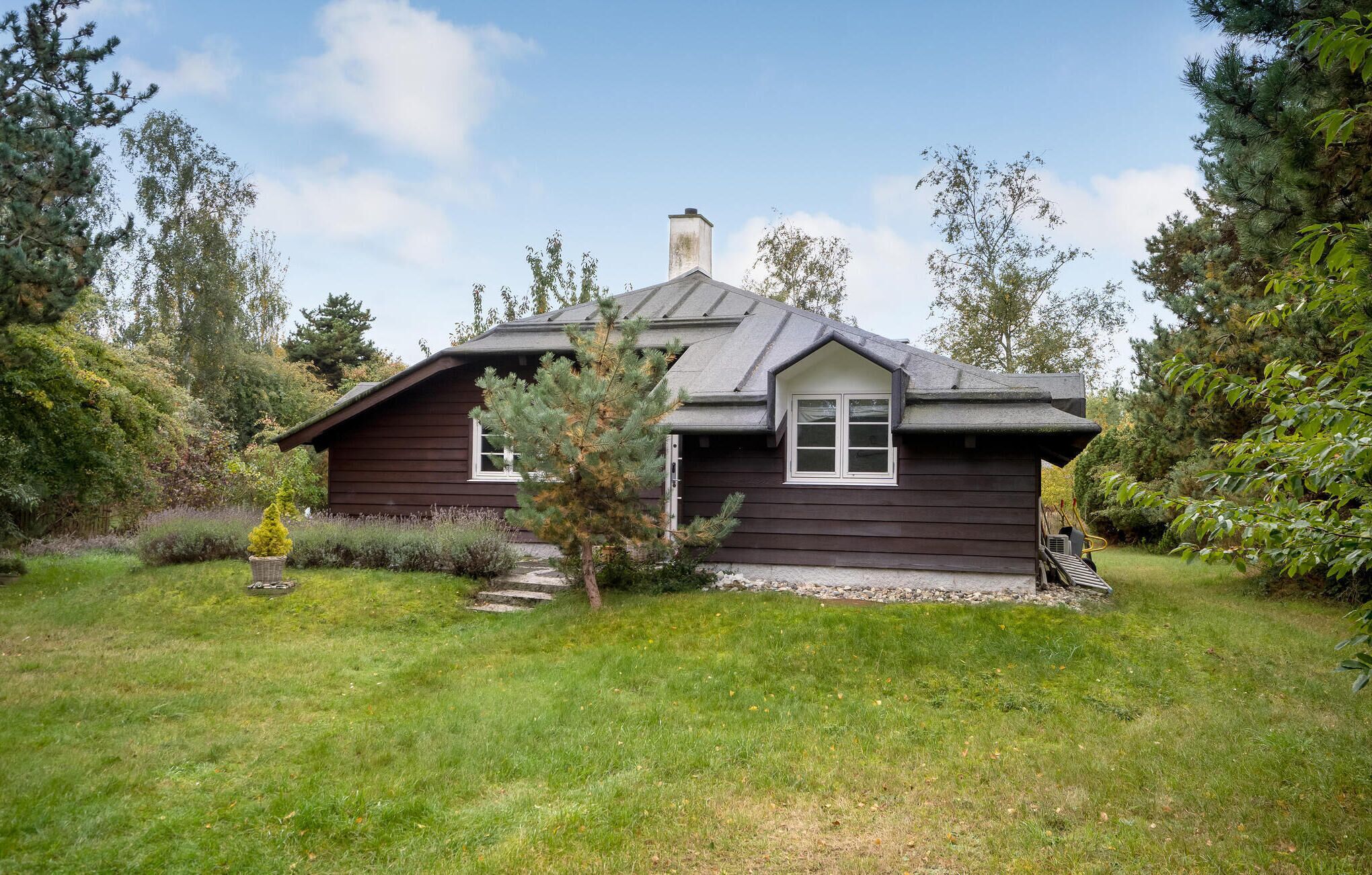 Een gelijkvloers huis met een donkerbruine gevel, een schoorsteen en een klein portaal met treden naar de ingang.