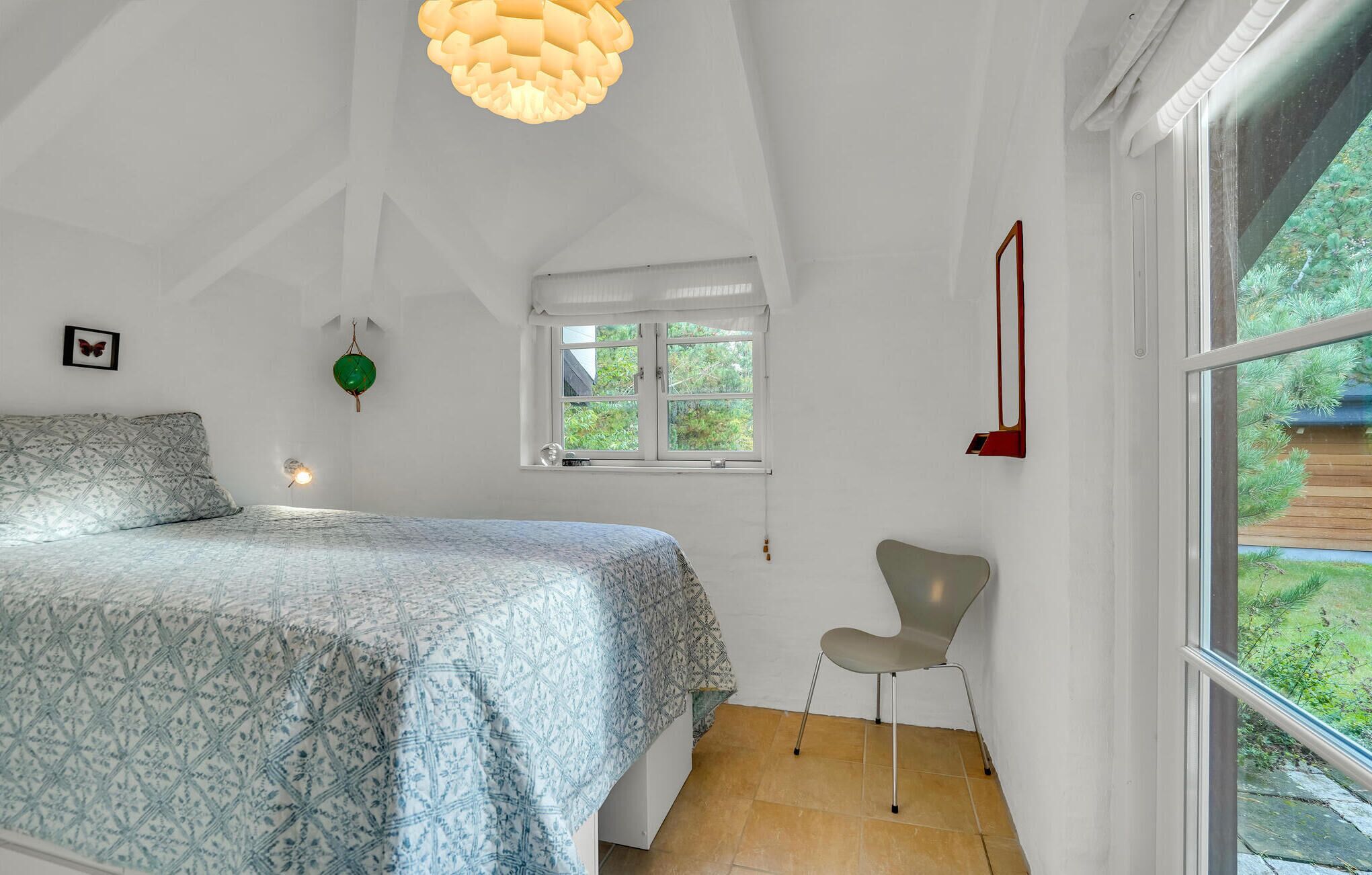 Ein Schlafzimmer mit Bett, Stuhl, Fenster und einer Pendelleuchte.