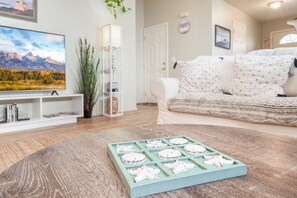 A living room with a wooden coffee table, a sofa, a TV, and a bookshelf. - Harris Beach Haven | Hot Tub, Theatre & Fire Pit (Brookings)