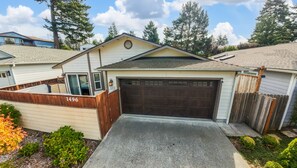 A single-story house with a garage, a wooden fence, and a driveway. - Harris Beach Haven | Hot Tub, Theatre & Fire Pit (Brookings)