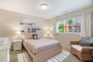 Ein Schlafzimmer mit einem Bett, zwei Nachttischen, einem Sessel, einem Fenster mit Vorhängen und Bildern an der Wand.