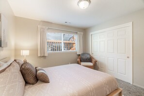 A bedroom with a bed, a chair, a window with curtains, a door, and a ceiling light. - Harris Beach Haven | Hot Tub, Theatre & Fire Pit (Brookings)