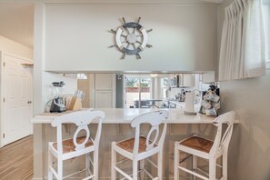 A kitchen with a central island, white chairs, a blender, and a ship's wheel decoration. - Harris Beach Haven | Hot Tub, Theatre & Fire Pit (Brookings)