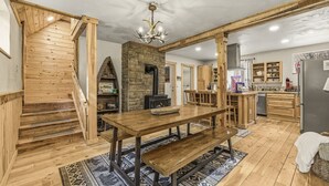 A wooden interior with a dining table, benches, a fireplace, and a kitchen area.