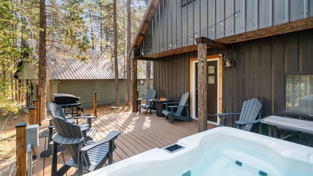 A wooden deck with outdoor seating, a hot tub, and a view of the surrounding forest.