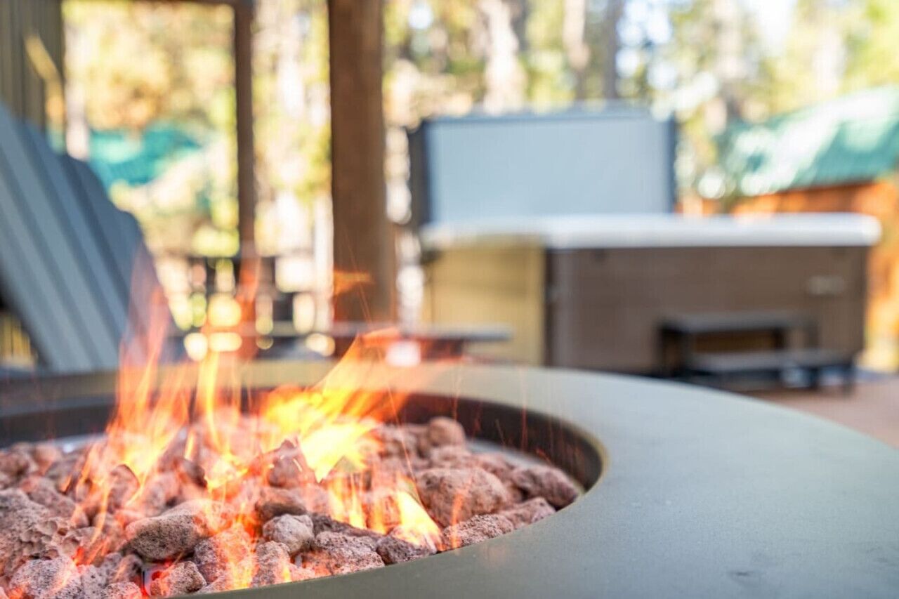 A fire pit with burning wood, surrounded by outdoor furniture and a TV screen in the background.