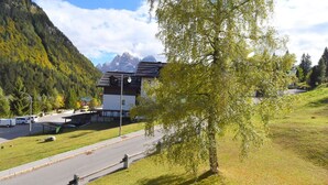 A building with a sloped roof, a parking area with vehicles, and a mountainous backdrop. - Lovely apartment for 2 guests with WIFI and TV (Ragoli)