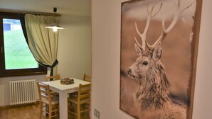 A dining area with a table and chairs, a window with curtains, and a painting of a deer on the wall. - Lovely apartment for 2 guests with WIFI and TV (Ragoli)