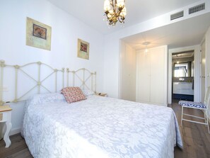 Relax in this serene bedroom with a large bed, nightstand, and wardrobe, featuring framed artwork and a chandelier.