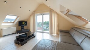 A modern loft bedroom with a large window, a flat-screen TV, a sofa, and a ceiling with skylights. - Lovely apartment for 4 guests with WIFI, TV and balcony (Bruges)