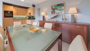 A modern kitchen with wooden cabinets, a glass dining table, and a painting on the wall. - Lovely apartment for 4 guests with WIFI, TV and balcony (Bruges)