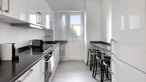 Una cocina moderna con encimera negra, armarios blancos, horno empotrado y una ventana que proporciona luz natural.