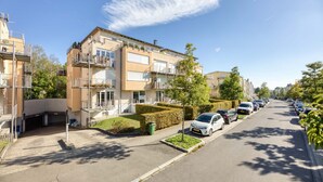 Une rue résidentielle bordée d’immeubles à plusieurs étages, avec des voitures garées et un ciel dégagé.