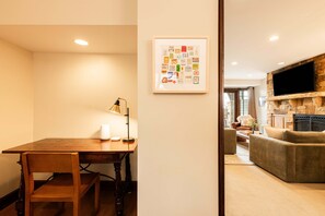 Un comedor con mesa y sillas de madera, una obra de arte enmarcada en la pared, y una sala de estar moderna con chimenea de piedra y televisor de pantalla plana.