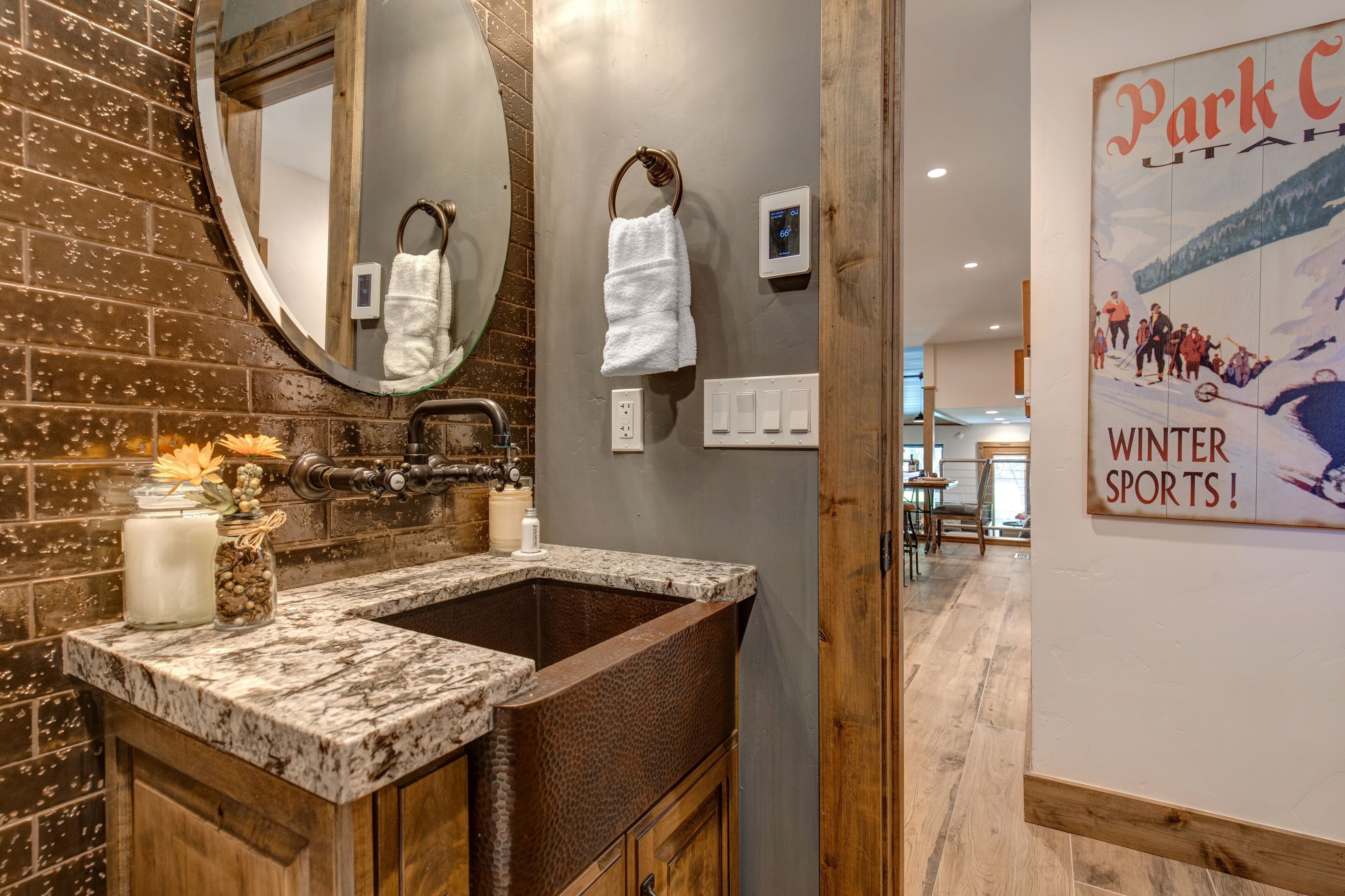 A bathroom with a brick wall, a round mirror, a wooden vanity, a sink, and a poster on the wall.