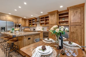 Une cuisine moderne avec des meubles en bois, des appareils en acier inoxydable et un coin repas agrémenté d’une vaisselle blanche, de verres et d’un centre de table décoratif en forme de pomme de pin.
