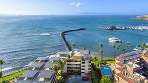 A coastal hotel with multiple buildings, a pier extending into the sea, and a marina with boats.