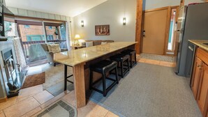 Una cocina con una isla grande, taburetes de bar, un refrigerador y un comedor con sofá y mesa.