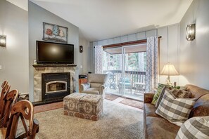 Cozy living room with a fireplace, comfortable seating, and a TV above, offering a view of the outdoors from the balcony.