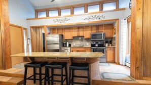 Una cocina con armarios de madera, una isla grande con taburetes, electrodomésticos de acero inoxidable y un diseño decorativo en el techo.