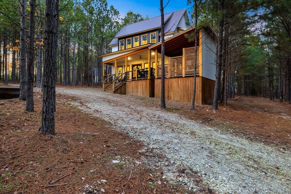 A two-story cabin with a covered porch and a small shed, surrounded by a forest. - Games, Hot Tub, Fire Pit, Close to Town, Pets, Triple C (Broken Bow)