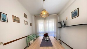 A dining area with a wooden table, chairs, a green sofa, and a chandelier. - Cosy apartment for 6 guests with TV and balcony (Rosignano Marittimo)