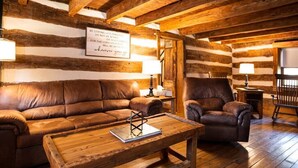 A log cabin interior with a brown leather sofa, a wooden coffee table, and a leather armchair.