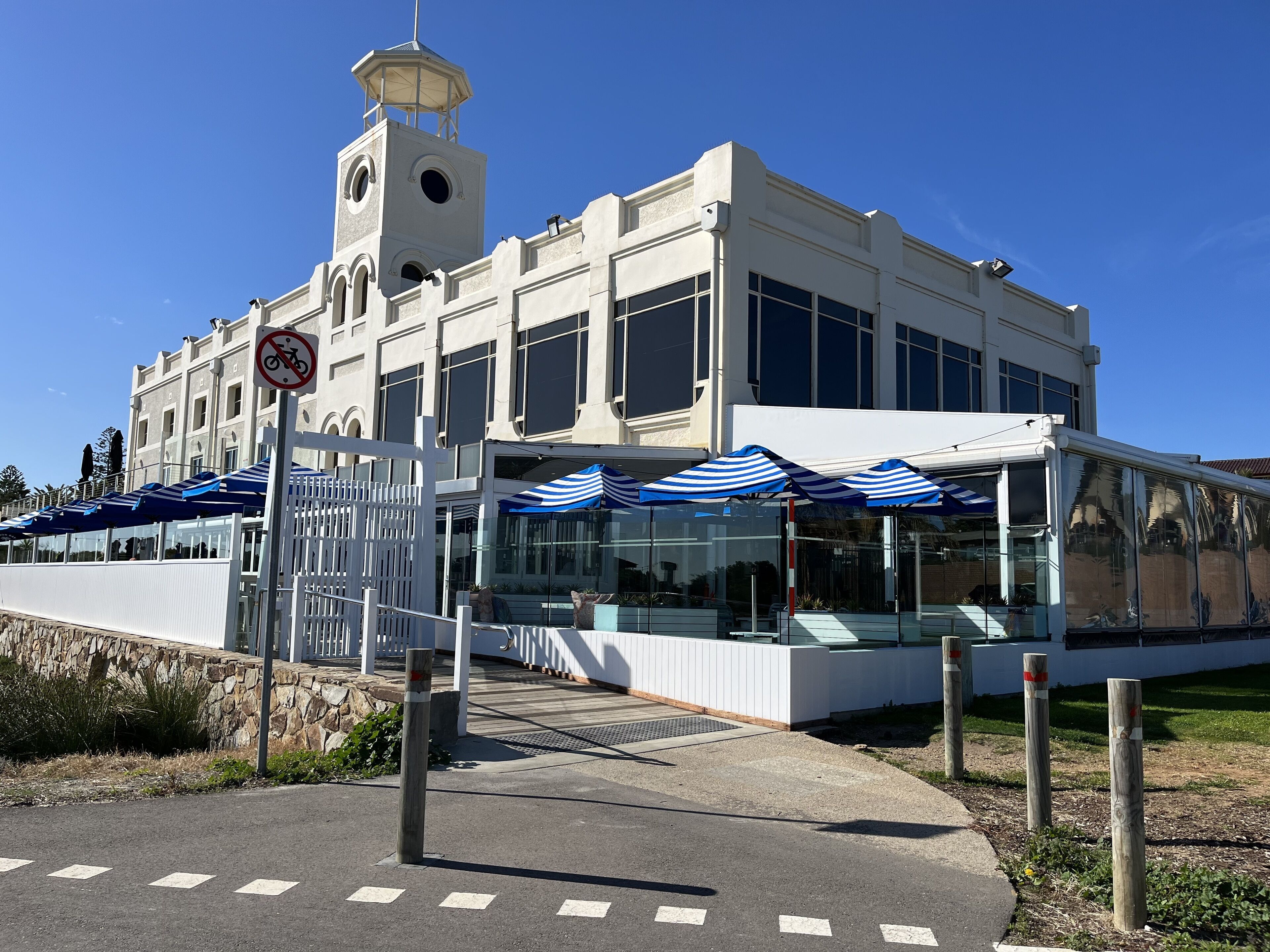 A building with a clock tower, large windows, and outdoor seating with umbrellas.