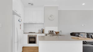 Una cucina moderna con mobili bianchi, forno integrato, microonde e orologio a parete.
