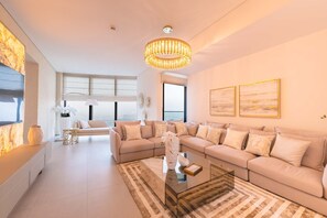 Ein geräumiges Wohnzimmer mit einer großen, L-förmigen beigen Couch, einem Glastisch und einem modernen Kronleuchter.