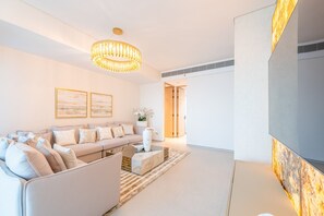 A modern living room with a beige sofa, a wooden coffee table, and a large flat-screen TV. There are two framed artworks on the wall and a decorative light fixture above the sofa.