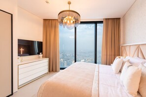 Quarto moderno com uma cama grande, uma televisão em uma cômoda e vista da cidade através de amplas janelas.