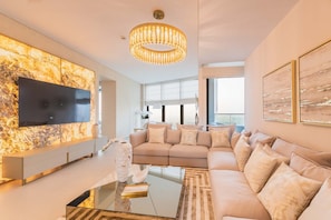 A modern living room with a large sectional sofa, a glass coffee table, a mounted TV, and a chandelier.