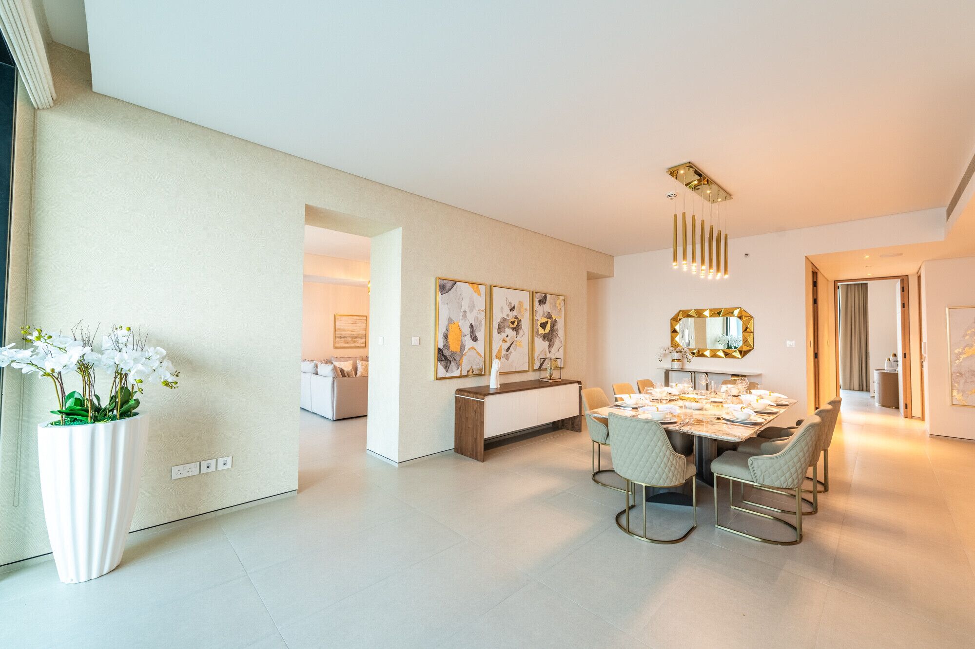 Un espace de repas moderne avec une table dressée pour six personnes, un canapé en arrière-plan et un grand miroir au-dessus de la table.