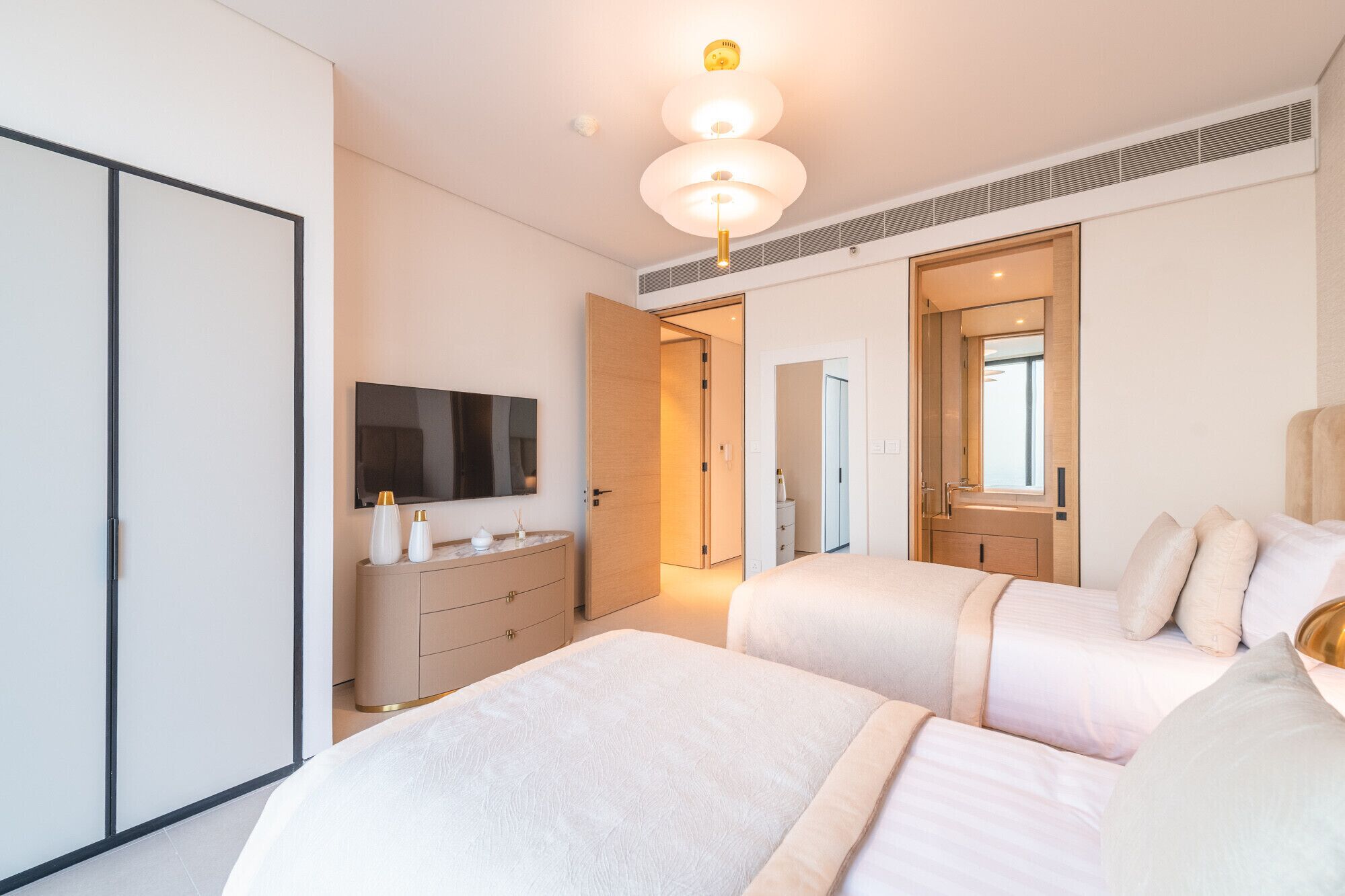 Quarto de hotel moderno com uma cama grande, televisão, cômoda e banheiro visível por uma porta aberta.