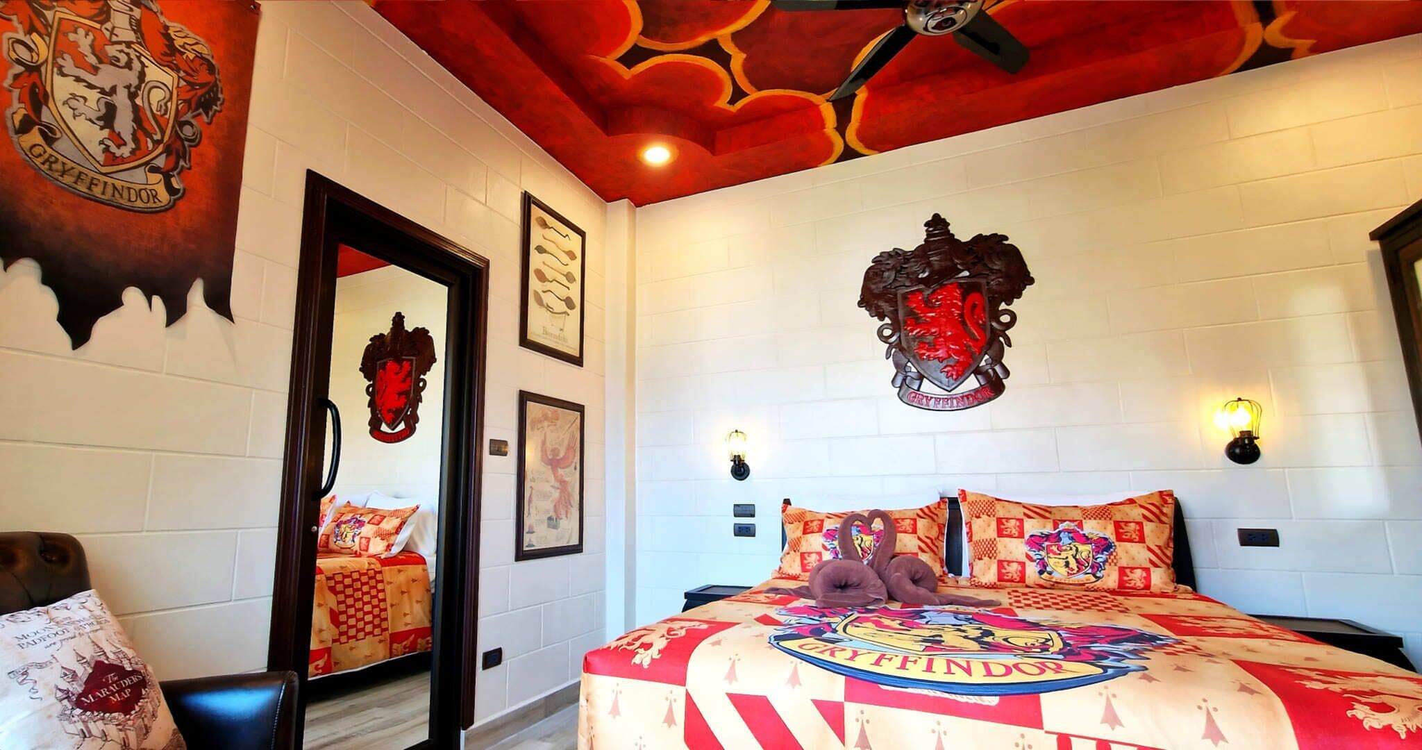 A bedroom with a Gryffindor crest on the wall, a large bed with a Gryffindor-themed duvet, and a mirror reflecting the room's decor.