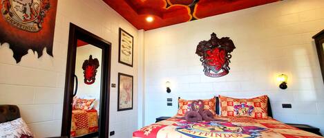 A bedroom with a Gryffindor crest on the wall, a large bed with a Gryffindor-themed duvet, and a mirror reflecting the room's decor.