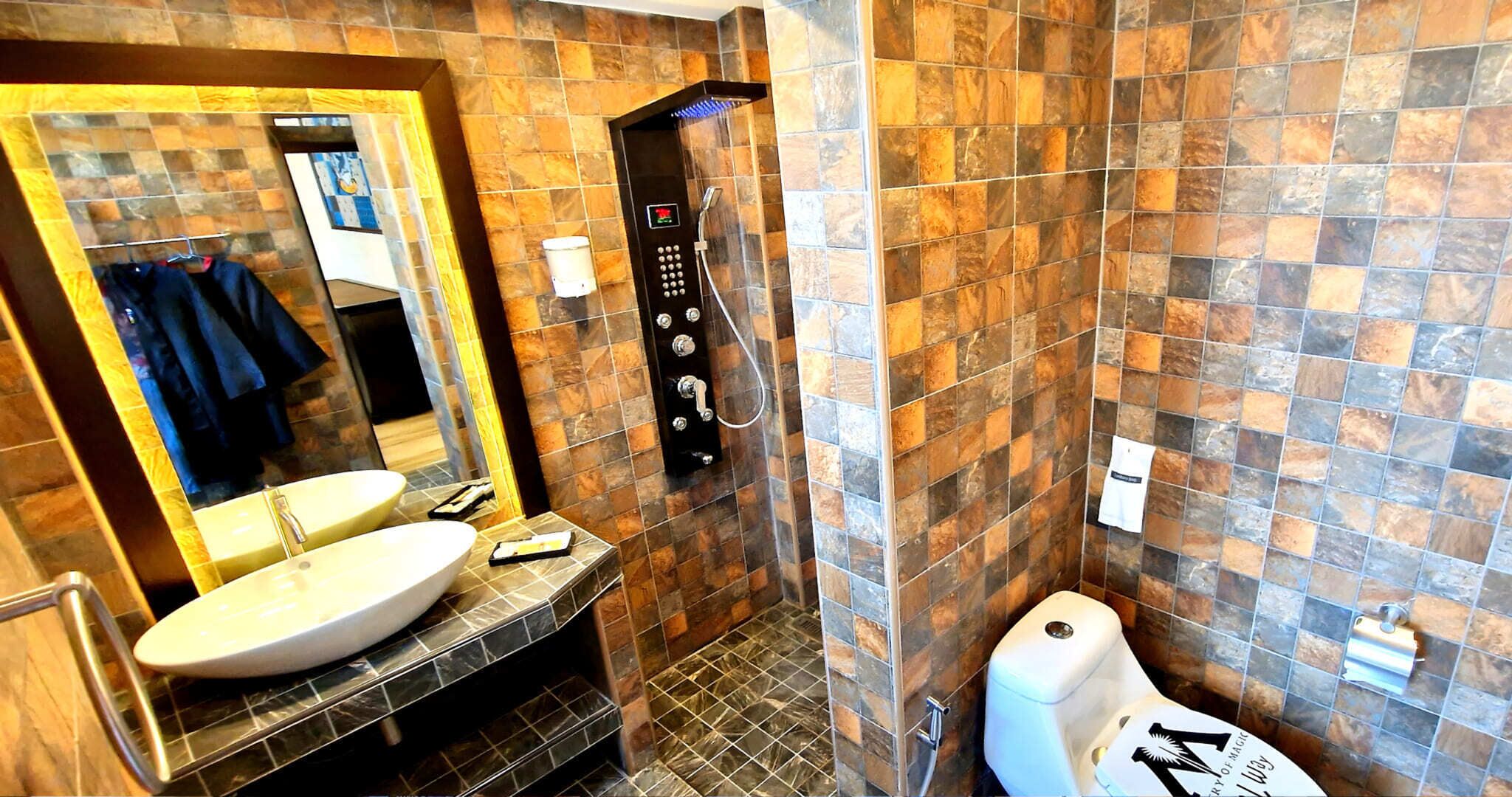 Et badeværelse med et stort spejl, en vask, en bruser med kontrolpanel og et toilet.