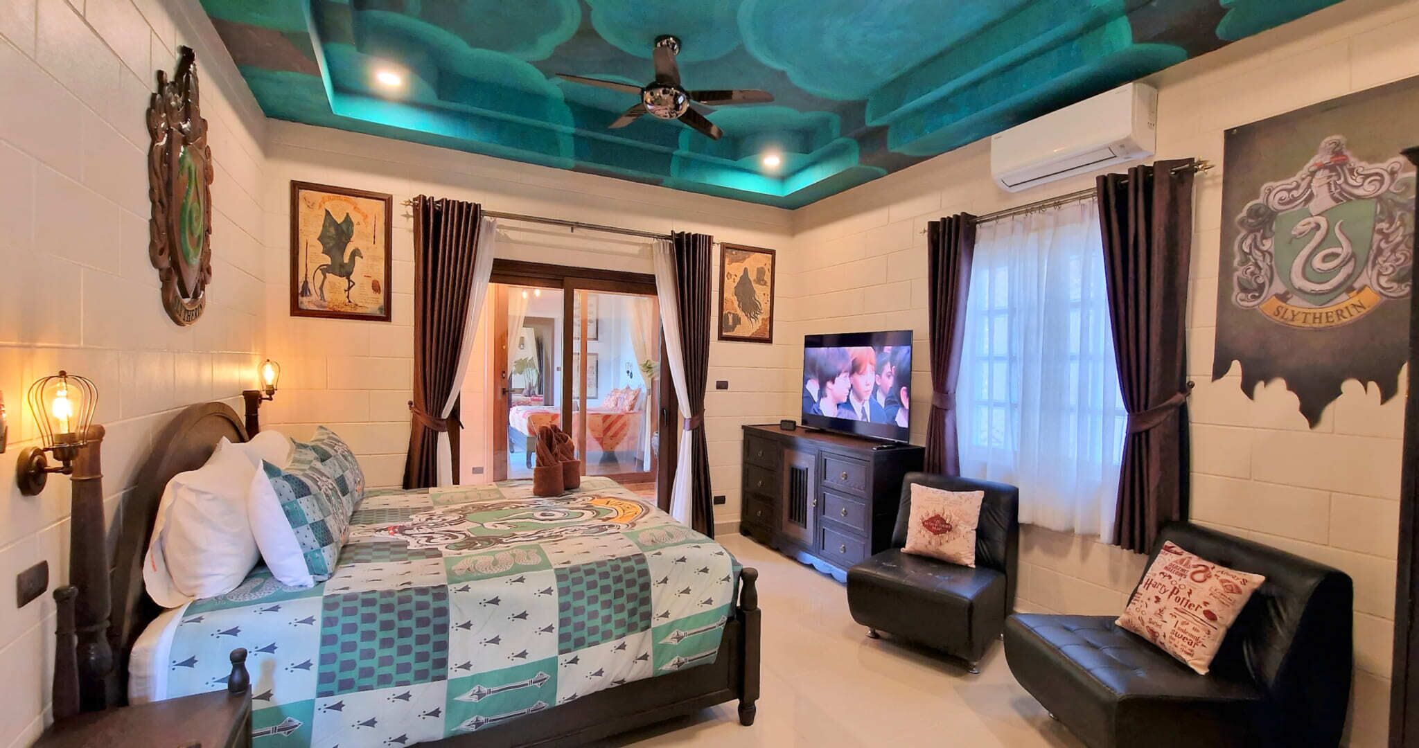 A hotel room with a bed, a TV, a sofa, and a ceiling fan.