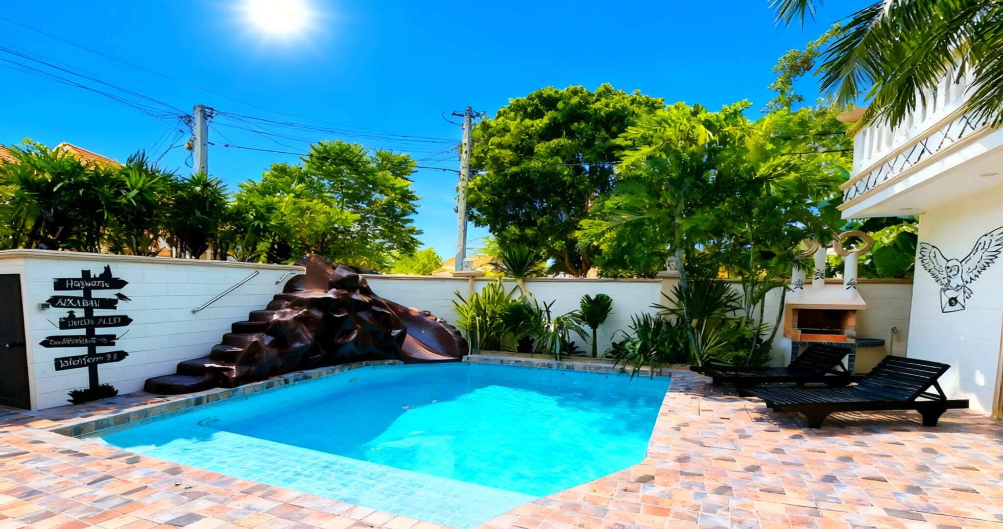 Una piscina con una cascada de rocas, rodeada por un patio empedrado y abundante vegetación.