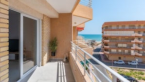 Ein Balkon mit Blick auf das Meer, eine Ziegelwand und eine Glastür zu einem Raum.