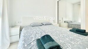 A modern bedroom with a large bed, a nightstand, a mirror, and a neatly made bed with towels. - Allegra 19 Ciudad Quesada by Villas&You (Ciudad Quesada)