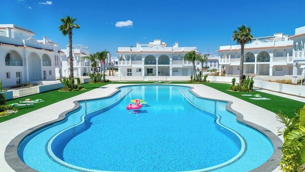 A swimming pool with a pink float, surrounded by white buildings with arched windows and balconies, and palm trees. - Allegra 19 Ciudad Quesada by Villas&You (Ciudad Quesada)