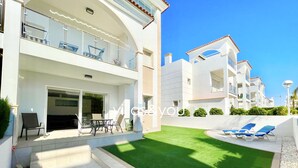 A modern hotel with a covered outdoor seating area, a well-maintained lawn, and a clear view of the adjacent buildings. - Allegra 19 Ciudad Quesada by Villas&You (Ciudad Quesada)