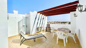 Une terrasse sur le toit avec une chaise blanche, une table et une pergola rouge.