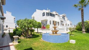 Un bâtiment blanc avec une fontaine au centre d’un jardin bien entretenu.