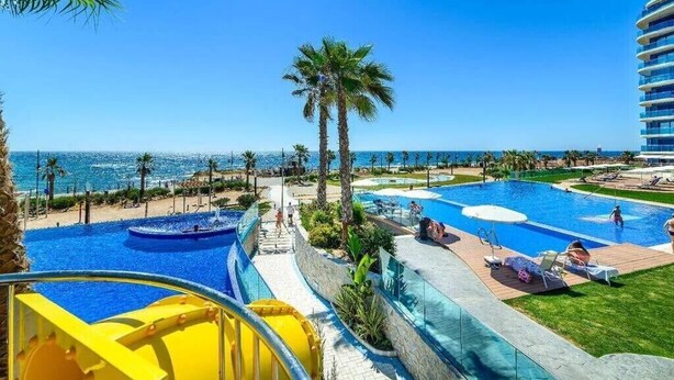 Een zwembadcomplex van een resort met meerdere zwembaden, palmbomen en uitzicht op de oceaan.