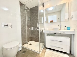 Ein modernes Badezimmer mit Duschkabine aus Glas, Toilette, Waschbecken mit Spiegel und Handtuchhalter.