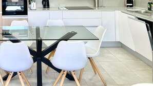 Una cucina moderna con un tavolo da pranzo in vetro, sedie bianche e forno a incasso.
